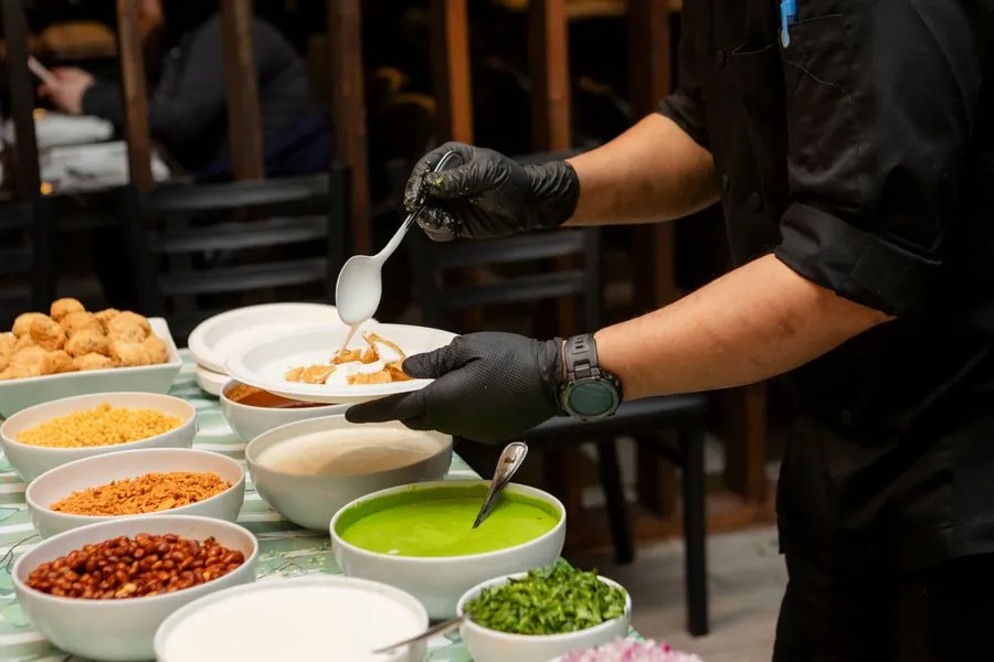 A cook in gloves plating chaat with chutneys at a clean counter
